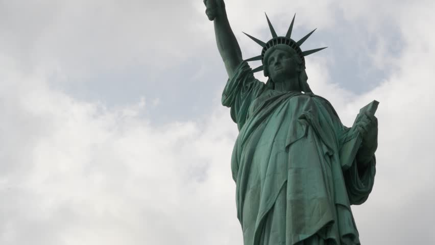 Statue of Liberty on Liberty Island, New York, United States. Blue cooper monument, symbol of democracy and patriotism near Manhattan, NYC USA. Clouds on sky. American independence. Torch and crown.