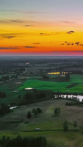 Sunset over lush green fields and tranquil waters, vibrant sky colors
