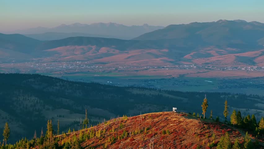 Mountain ridge landscape overlooking Missoula Montana valley, camper parked in bottom corner, aerial