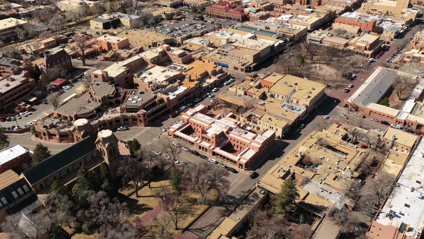 A sweeping wide shot captures the heart of Santa Fe’s tourism district during a clear winter day. The stone towers of the basilica stand in contrast to the surrounding Pueblo-style buildings.