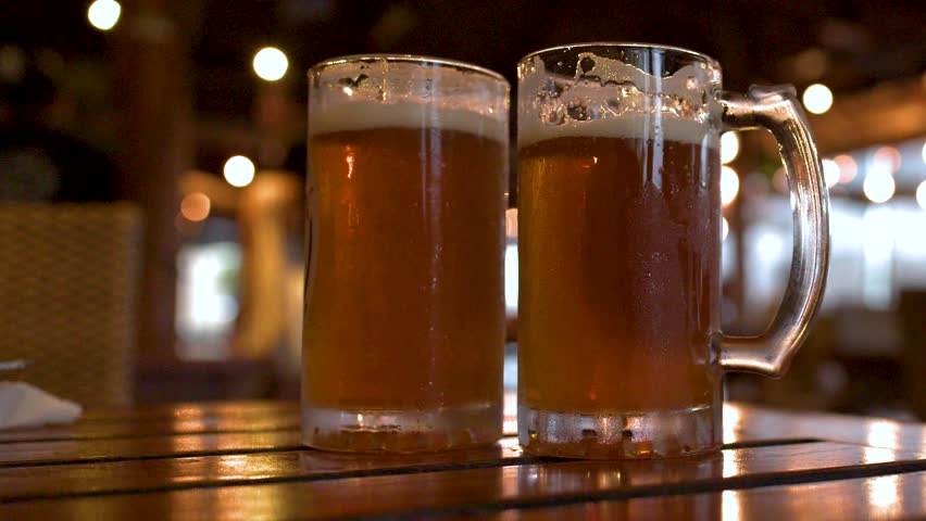 Close-up of cold beer mugs with condensation on a wooden table in a dim bar