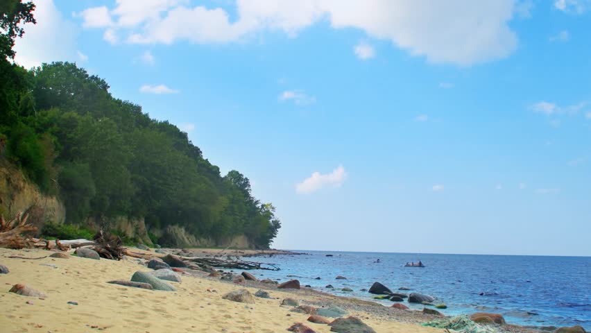 A sandy seashore with a tree-lined slope. Summer panorama of the beach with Mediterranean nature. Trees and bushes on the slope by the water.