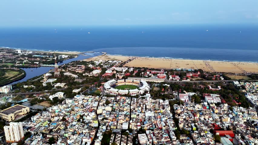 Aerial perspective of Chennai’s Marina coastline, highlighting the wide sandy beach, gentle ocean waves, and dense urban skyline running parallel to one of the longest urban beaches in the world.