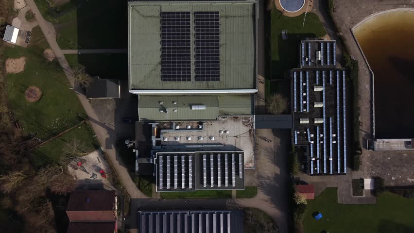 Aerial top down view of modern sports and recreation complex in United States with building with rooftop solar panels, nearby soccer field, outdoor pool and surrounding park area. Spring season.