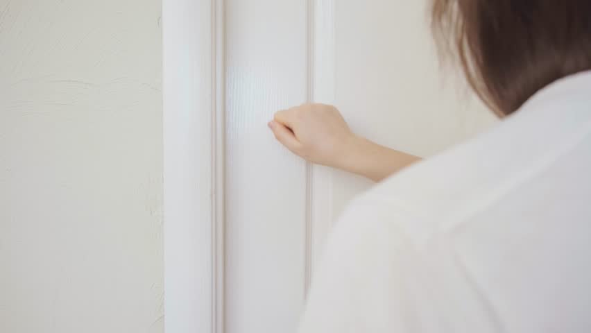 Back view of woman knocking on closed white wooden door waiting for answer visiting home or calling someone behind the door