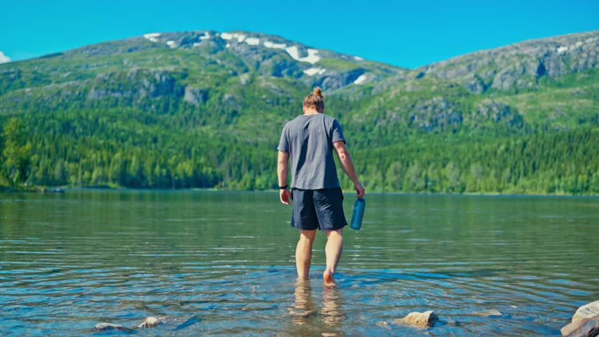 A Person Wading in a Lake While Holding a Bottle in Mosjøen, Norway - Static Shot