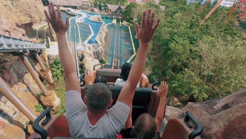 People raising hands on roller coaster drop in amusement park