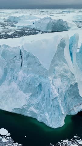 Aerial perspective of a majestic iceberg in Greenland, vertical video showing the scale of the arctic ice. Massive iceberg floating in the cold arctic ocean