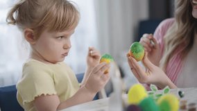 Child paints Easter egg with focused expression. Mother smiles, guiding child's hands gently. Bright yellow eggs sit beside them. Joyful family moment during spring celebration. Perfect for parenting - Powered by Shutterstock - Get 15% off with code: PIKWIZARD15