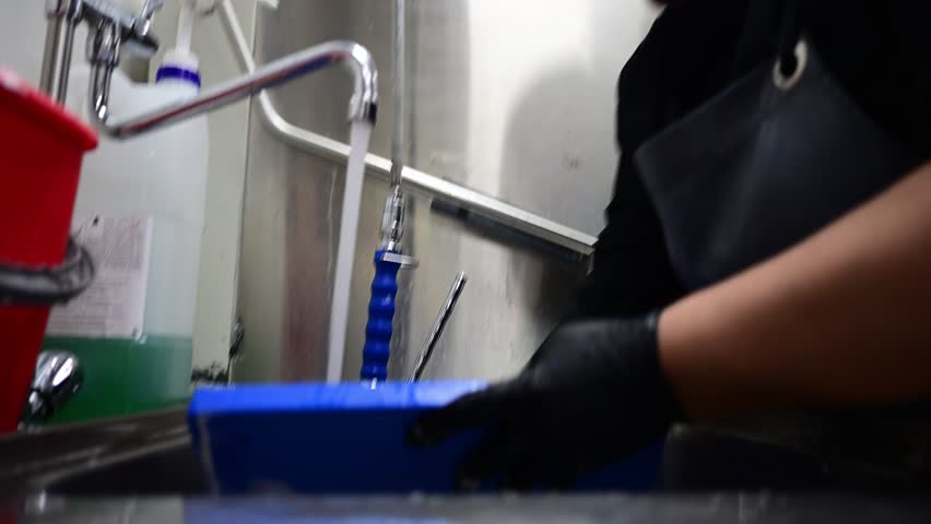 Restaurant employee washing dirty pots in a commercial kitchen sink