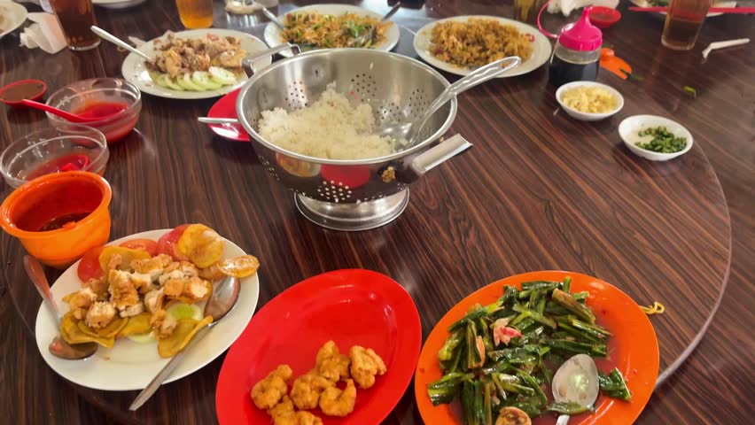 Chinese restaurant table scene of rice,chow mein fried noodles,egg foo young,fried fish and shrimp or prawn, Stir-fried Chinese Greens and steamed chicken with fried garlic on a rotating wooden table.