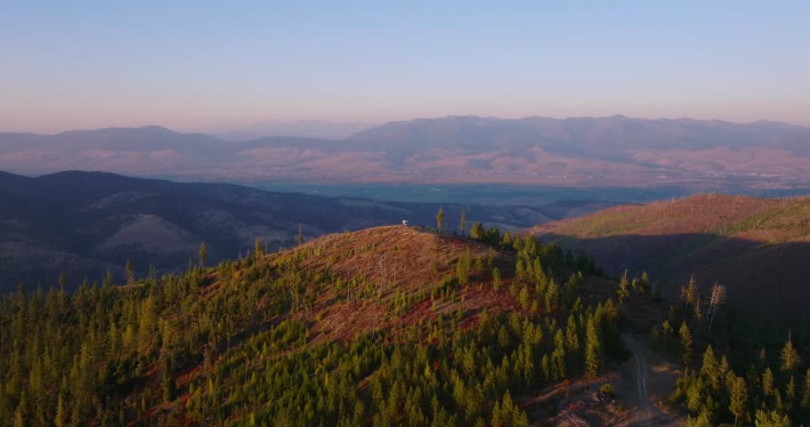 Evening aerial of rolling mountains around Missoula Montana, camper at end of long road