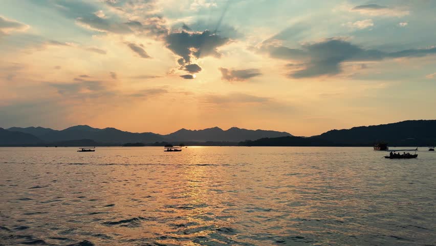 Sunset at West Lake in Hangzhou China with boats on the water and hills in the distance, warm light bathes the landscape