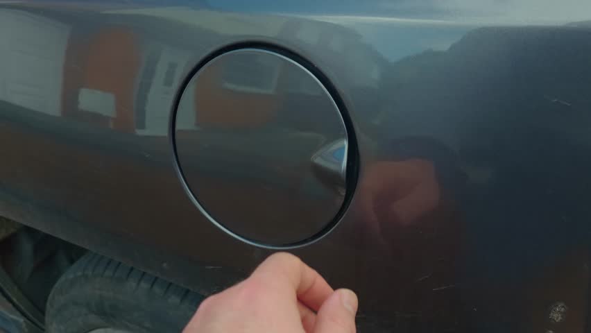 Driver hand opening car fuel cap then gesturing no refusal due to expensive gasoline prices. Vehicle fuel tank lid and petrol cap close up with finger signaling negative decision about refueling