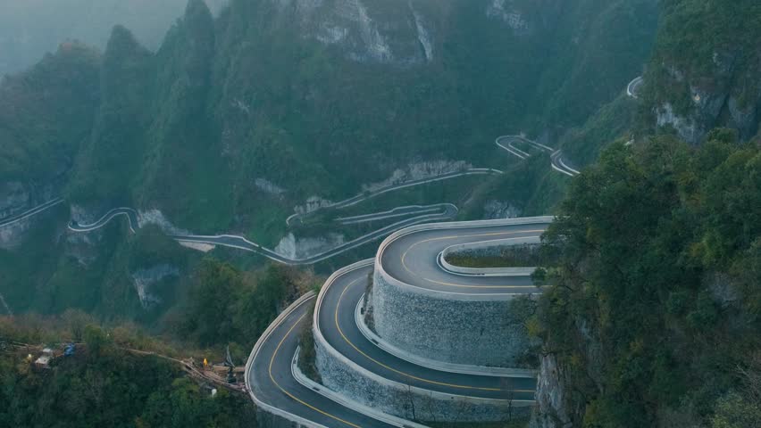 Mountain road landscape of Tianmen Mountain Road with hairpin turns through lush karst peaks and forest valleys at sunrise.in Tianmen Mountain National Park, Zhangjiajie, Hunan, China