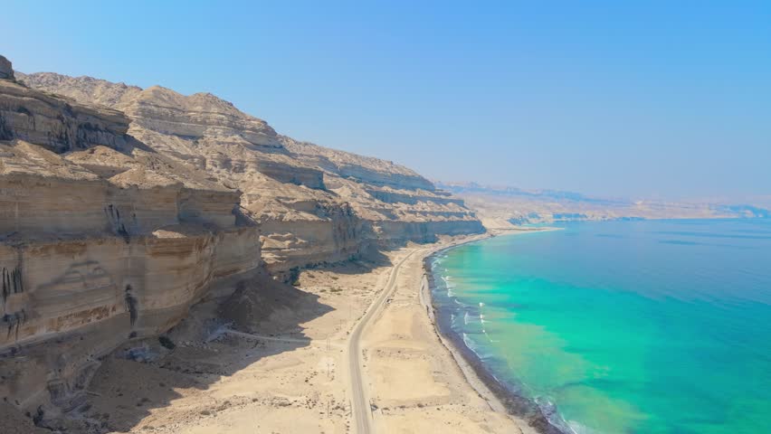 Aerial view of a coastal road stretching between steep rocky cliffs and turquoise ocean water near Salalah, Oman.