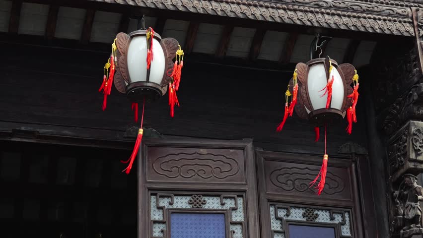 Two lanterns hang outside a building with intricate carvings and traditional Chinese architectural details.