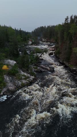 Turtle Falls on the Manigotagan River in Manitoba flowing over Canadian Shield granite. A vertical aerial view from downstream shows whitewater rapids and a riverside tent in summer boreal forest.