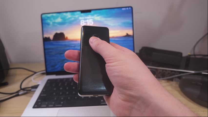 Hands operating simple keypad mobile phone placed near modern laptop computer, representing coexistence of older communication devices, current digital technology in everyday technological environment