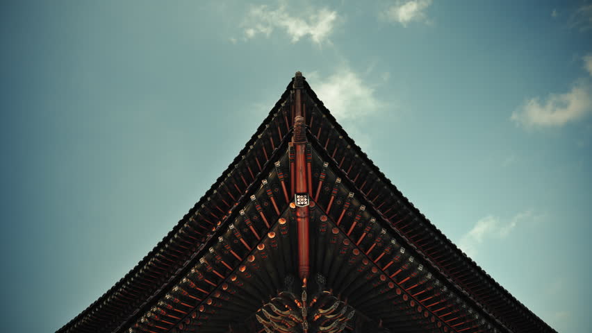 Cinematic low angle view of traditional Korean temple roof in Seoul, South Korea with clouds drifting across blue sky