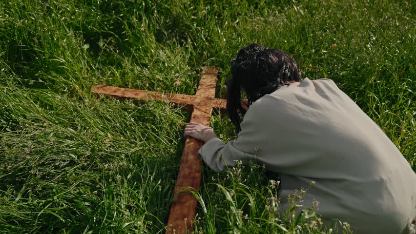 Person kneeling in grass holding wooden cross symbolizing Jesus suffering and Christian faith during Easter passion reflection