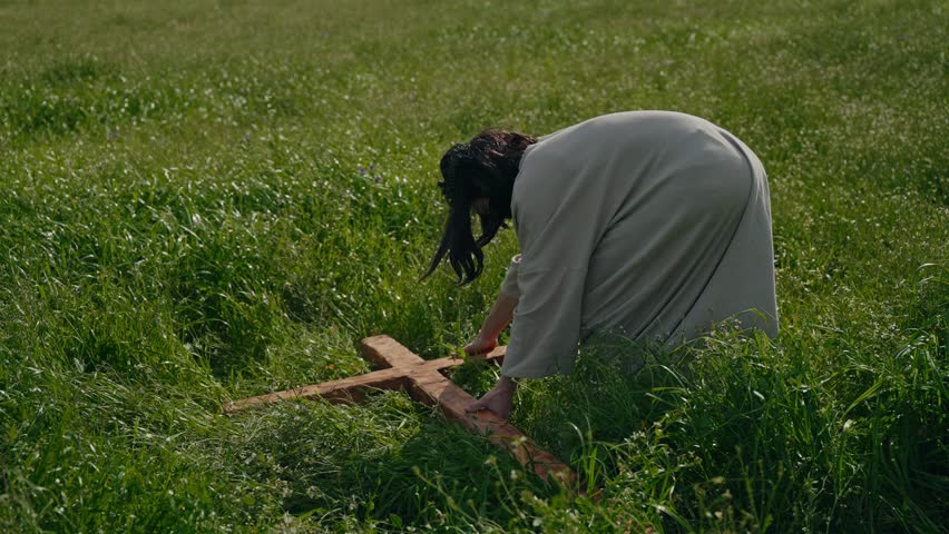 Jesus lifting wooden cross from grass and placing it on shoulder slow motion Easter crucifixion reenactment