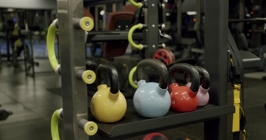 Colorful iron kettlebells of different weights and colors are standing on a shelf in a modern gym, ready for a functional cross-training workout to build strength and endurance