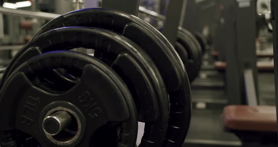 Close-up of heavy black barbell weight plates organized on a chrome rack in a modern fitness gym, showing equipment for strength training and bodybuilding with a blurred background