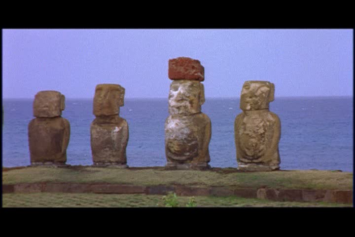 MS row of moai statues near coast on Easter Island, Chile. Ocean and cliffs in background.