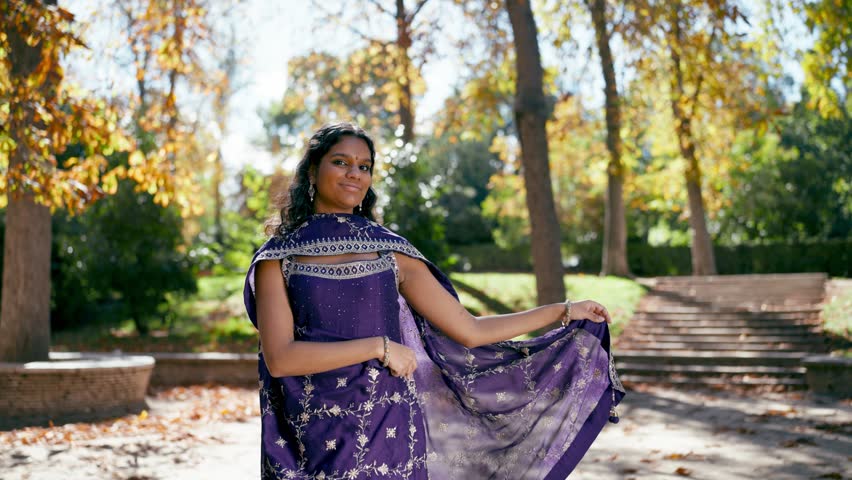 Beautiful young indian woman with a bindi smiling and dancing gracefully in a park. She wears a traditional purple sari during a celebration