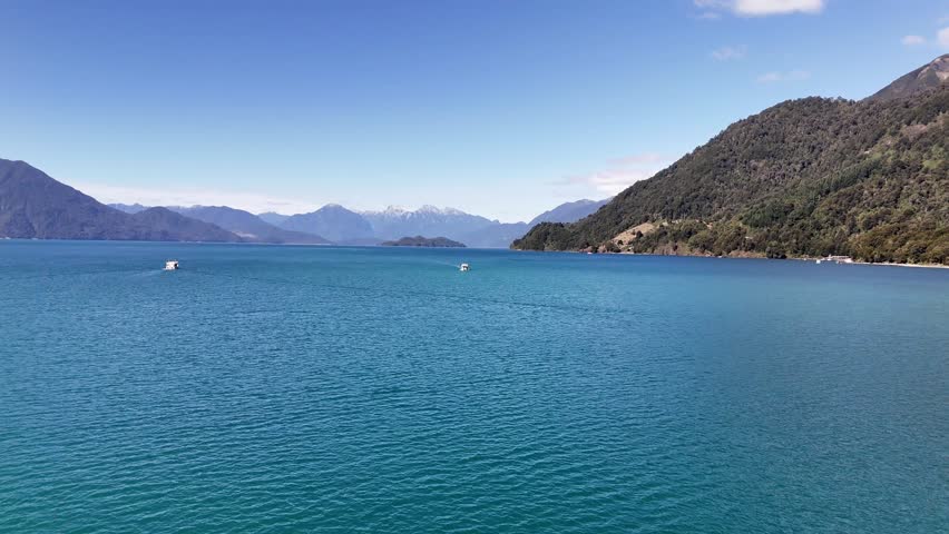 Aerial moves forward over the emerald waters of Lake Todos los Santos in Vicente Pérez Rosales National Park, featuring several ferries and the dramatic Andean mountain horizon