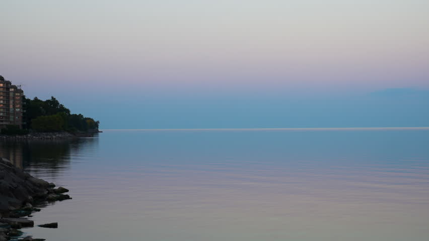 Blue and pink pearl-like sunset colors over Lake Ontario horizon with small landmass. Burlington, Ontario.