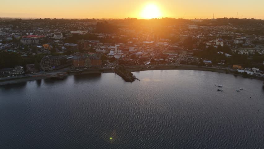 Cinematic aerial approaching from a distance over Lake Llanquihue and tilting down to reveal a close-up view of the tourist piers and waterfront promenade of Puerto Varas, Chile