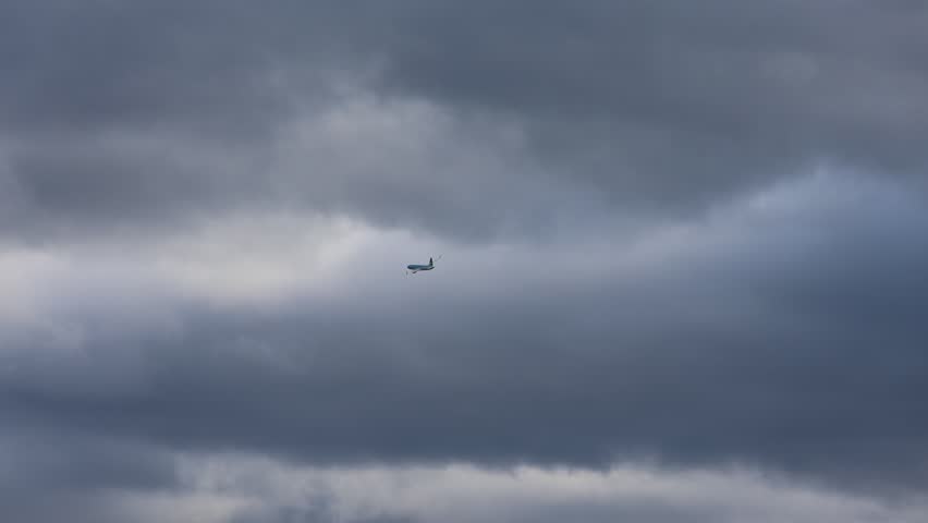 A large aircraft performing a turn, captured from a good distance with a dark cloudy sky in the background.