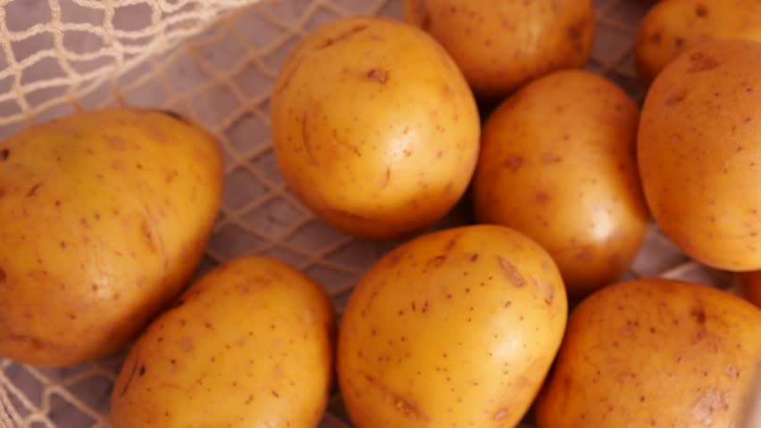 Fresh raw yellow potatoes in a cream reusable mesh produce bag on a light gray countertop, ready for a healthy meal