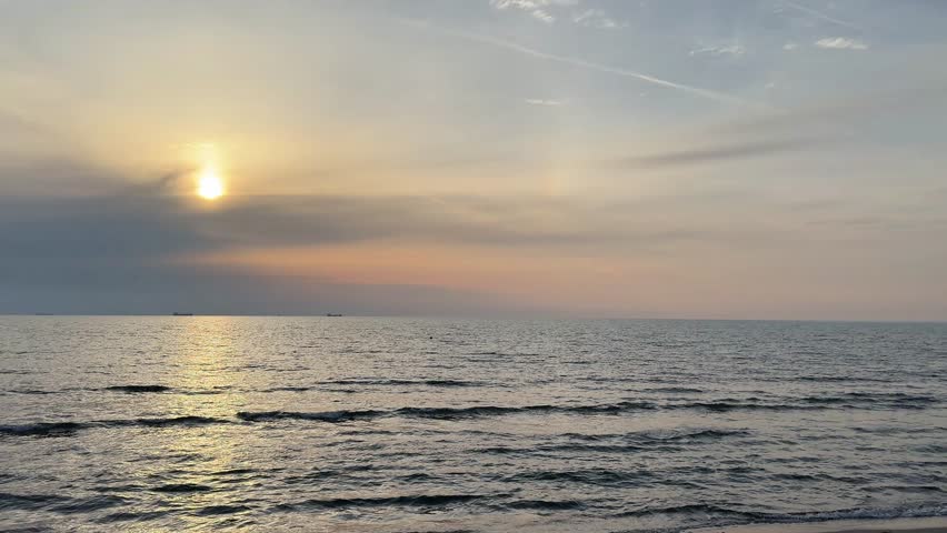 Sun setting above calm Adriatic Sea waves with warm golden hour light. Peaceful marine landscape with wide horizon and reflective water surface.