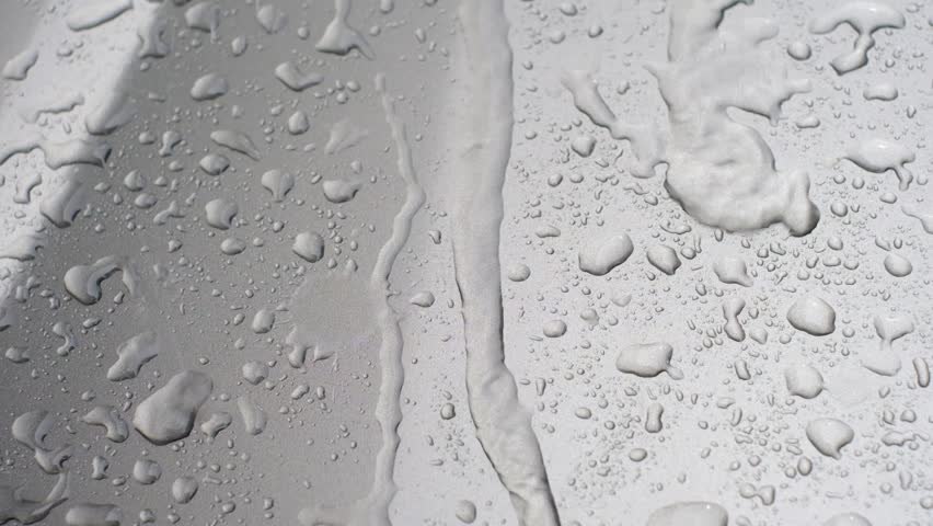 A wet surface with water droplets on it. The droplets are scattered all over the surface, creating a sense of movement and energy. Scene is one of motion and fluidity