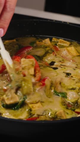 Green curry tofu soup cooking. Thai green curry soup in a white bowl on a white plate with dark background. Flat lay, overhead