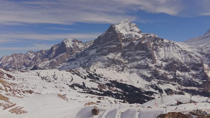 Aerial view of the summit station Grindelwald First, surrounded by massive snowy mountains.