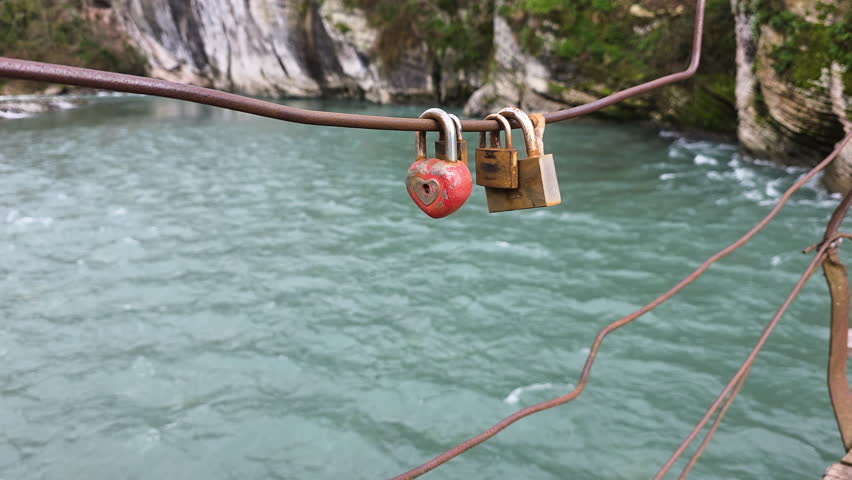 Heart shaped love lock symbolizing eternal romance and commitment swaying over a flowing river