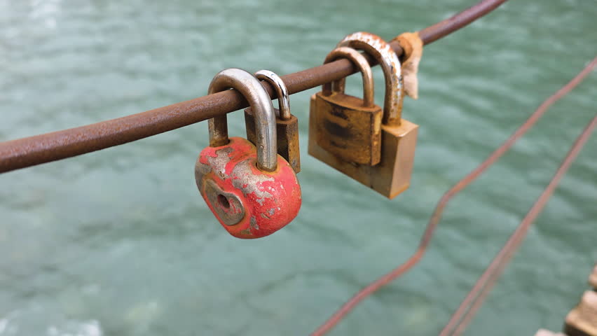 Heart-shaped padlock symbolizing eternal love hanging on a bridge railing with flowing river water in the background