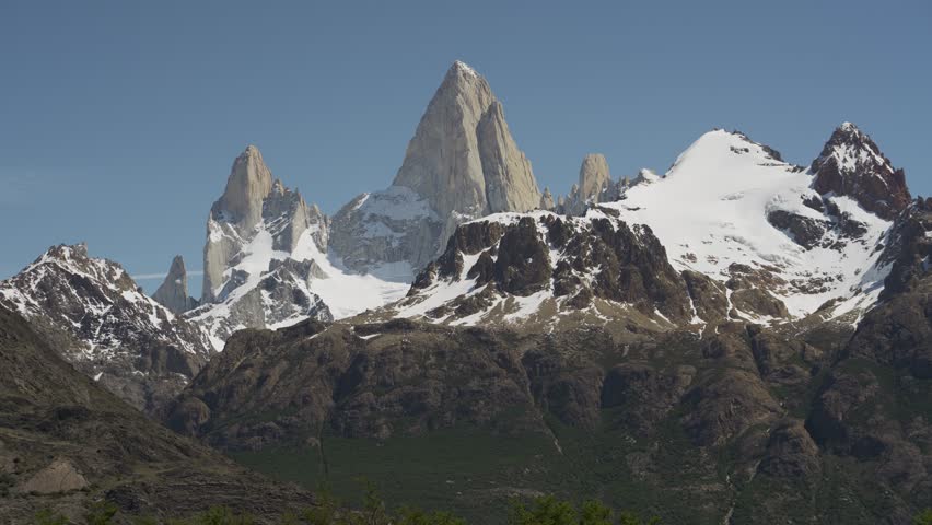 Close up of a man walking in front of sharp snowy mountain peaks of Mount Fitz Roy focus. Patagonia, Argentina