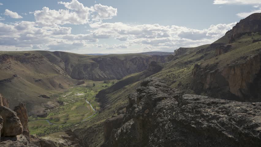 Man standing on a rocky ledge overlooking canyon vast mountain valley in nature in Parque Patagonia. Santa Cruz, Argentina