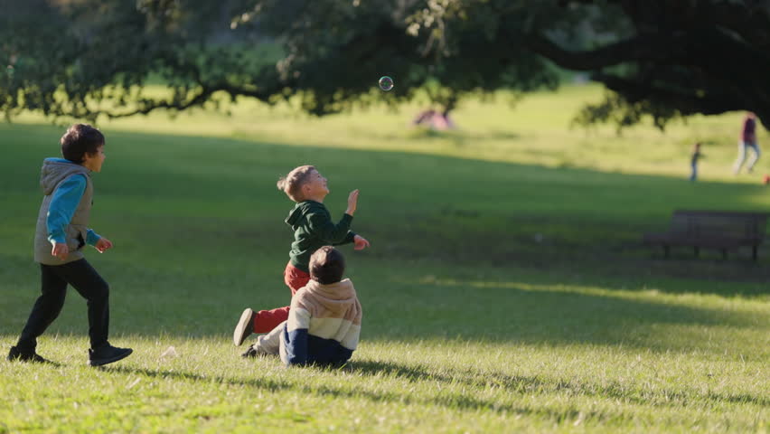 Three children running and playing with bubbles in the park