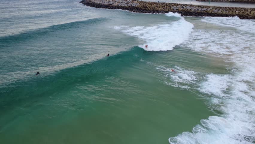 Two surfers catching waves as the sun shines on the ocean, with one surfer dramatically flying off the end of a wave like Superman. The footage captures the excitement, action, and dynamic energy of surfing in vibrant blue coastal waters.