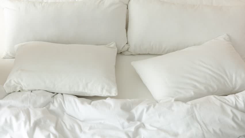 Man arranging pillows on bed indoors, closeup
