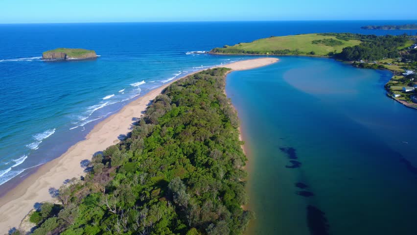 Aerial view flying over a scenic cape where a river meets the ocean, with a small island nearby. The vibrant blue waters of the river and ocean converge, surrounded by lush coastal land, showcasing the dramatic beauty of the natural landscape from above.