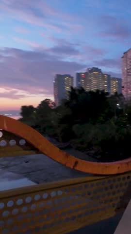 Sunrise over a calm river with reflections of colorful clouds and city buildings in the early morning. Silhouetted high-rise apartments and urban skyline create a peaceful dawn atmosphere in George Town, Southeast Asia. Tranquil waterfront scene with still water reflecting the sky during golden hour.