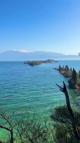 Scenic vertical view of a vast blue lake with snow-capped mountain peaks in the distant horizon under a clear sky.