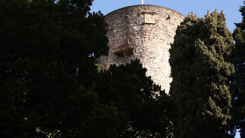 Italian tricolor flag waving from a historic stone tower in Bergamo Alta against a clear sky